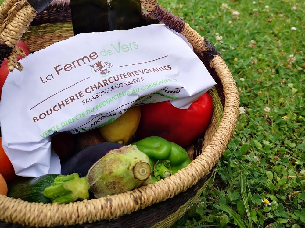 Panier avec légumes, bouteille d'huile et produit de la Ferme de Vers (emballé dans un papier estampillé Ferme de Vers) sur de la pelouse